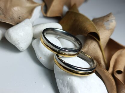 Pair of wedding rings in a combination of silver & gold color on a polished surface (CODE: 50001)